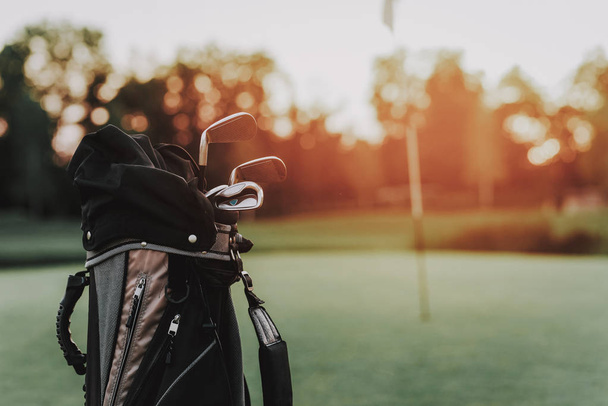 Golf Sticks in Black Bag on Green Field with Flag. Green Grass. Sport in Summer Concept. Outdoor Fun Concept. Flag on Stick. Sunny Day. Sport on Field Concept. Steel Golf Stick. Black Bag. - Фото, изображение