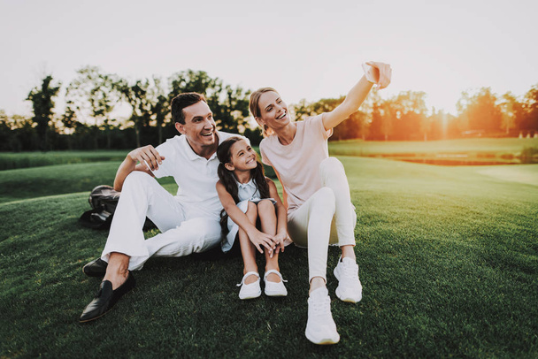 Happy Young Family Sitting on Golf Field in Summer. Relaxing in Golf Club. Sports in Summer. Outdoor Fun in Summer. Family Fun. Healthy Lifestyle Concept. Little Girl. Green Grass. - Zdjęcie, obraz