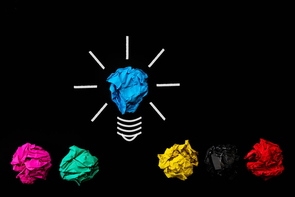 Inspiratie en geweldig idee concept. lampje met verfrommeld kleurrijke papier op zwarte achtergrond. - Foto, afbeelding