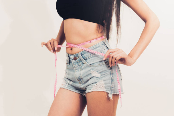 Mujer delgada joven mide su cintura midiendo cinta después de la dieta contra fondos blancos. Concepto de éxito de pérdida de peso
. - Foto, imagen