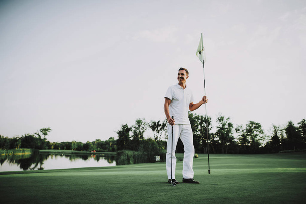 Young Man in White Clothes Playing Golf on Field. Relaxing in Golf Club. Sports in Summer. Outdoor Fun in Summer. Happy Young Man. Healthy Lifestyle Concept. Man it White Shirt. Green Grass. - 写真・画像