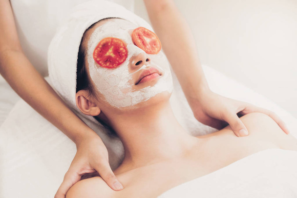 Mooie vrouw met een gezichtsmasker behandeling met tomaat crème extract tonen aanspraak op behandeling van de natuur. Anti-veroudert cosmetologie, gezichtshuid zorg en luxe levensstijl concept. - Foto, afbeelding