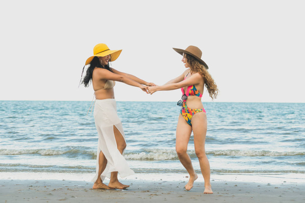 Glückliche Frauen in Bikinis tanzen im Sommerurlaub gemeinsam am tropischen Sandstrand. Lebensstil. - Foto, Bild