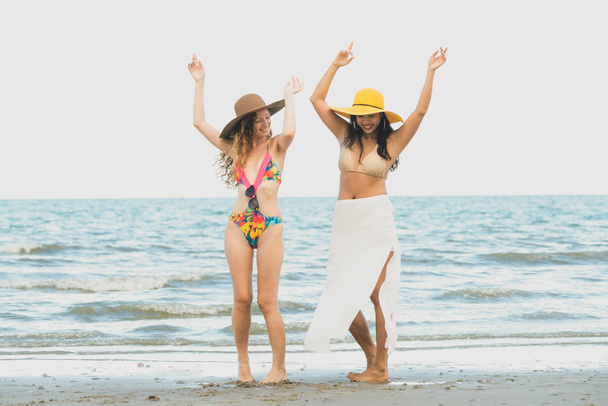 ビキニ姿の幸せな女性は夏休みに熱帯の砂浜に一緒に踊る。旅行のライフ スタイル. - 写真・画像