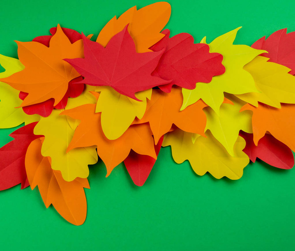Leaves of paper autumn. Red, yellow and orange leaves. Place for recording. Green background. - Foto, Bild