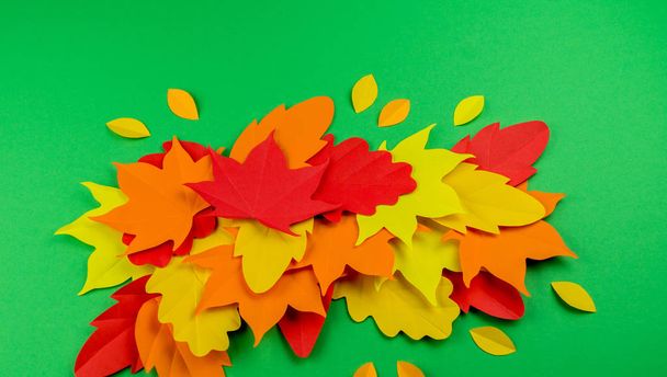 Leaves of paper autumn. Red, yellow and orange leaves. Place for recording. Green background. - Фото, изображение