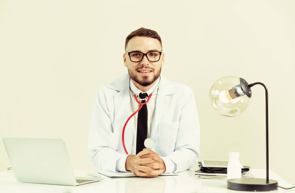 glücklicher männlicher Arzt am Schreibtisch im Krankenhaus, der am Laptop arbeitet. medizinisches Gesundheitskonzept. - Foto, Bild