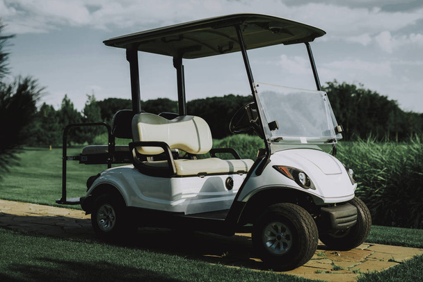 White Little Cart on Golf Field in Sunny Day. Healthy Lifestyle Concept. Golf Club. Sports in Summer. Vehicle on Field. Family Holiday. Outdoor Fun in Summer. Sunny Day. Electric Car. - Zdjęcie, obraz