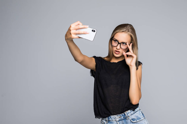 Usměvavá mladá dívka dělat selfie foto na smartphone za gray - Fotografie, Obrázek