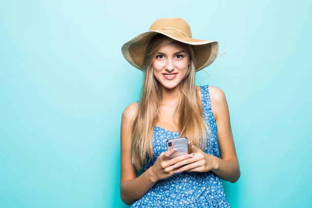 Moda donna sorridente utilizza smartphone indossando cappello di paglia su sfondo blu
 - Foto, immagini