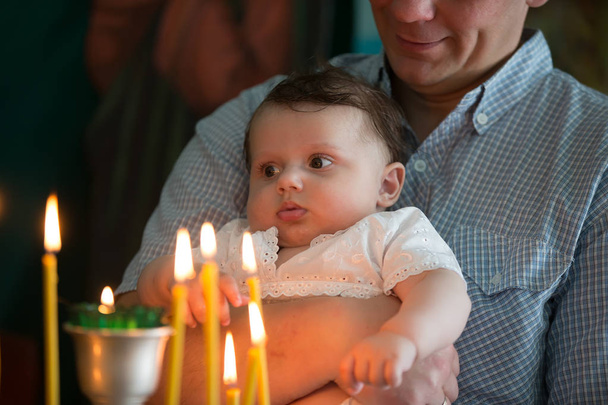 父の手は、教会の彼の腕で赤ちゃんを保持します。子供を見て寺の燃焼蝋燭。教会の子供 - 写真・画像