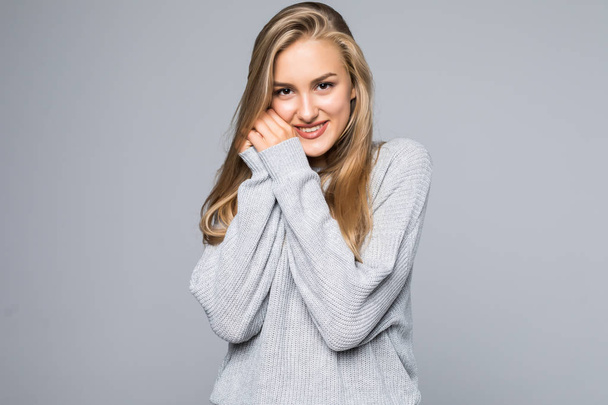 Porträt einer glücklich lächelnden Frau im Pullover mit den Händen vor dem Gesicht, die isoliert auf dem grauen Hintergrund wegschaut - Foto, Bild