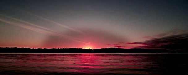 Ένα θεαματικό εμπνευσμένη λαμπρά χρωματισμένα κόκκινα και γκρι θολό θάλασσα νερό τροπικό πανοραμική sunrise Θαλασσογραφία που χαρακτηρίζουν τις σκιαγραφίες με αντανακλάσεις του νερού στον ωκεανό. Κουίνσλαντ, Αυστραλία. - Φωτογραφία, εικόνα