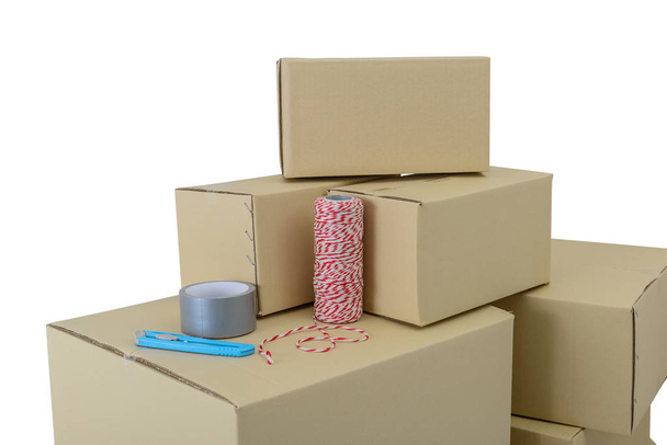 Cajas de cartón en cajas apiladas de diferentes tamaños, cinta adhesiva, cuerda y cortador aislados sobre fondo blanco con camino de recorte
 - Foto, Imagen