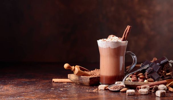 Cocoa with cream, cinnamon, chocolate pieces and various spices on a brown background. Copy space for your text. - Photo, Image