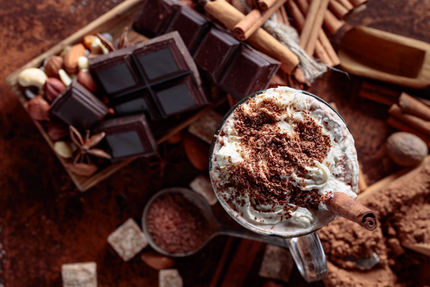 Cocoa with cream, cinnamon, chocolate pieces and various spices on a brown background. Top view. - 写真・画像