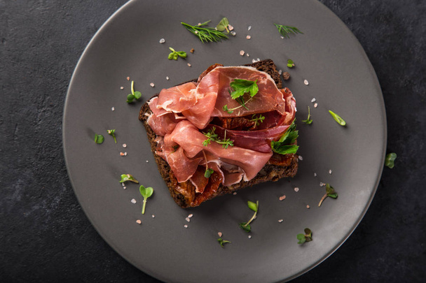 open sanwiches with dark rye bread, prosciutto and sun dried tomatoes, black background, top view, - Photo, Image