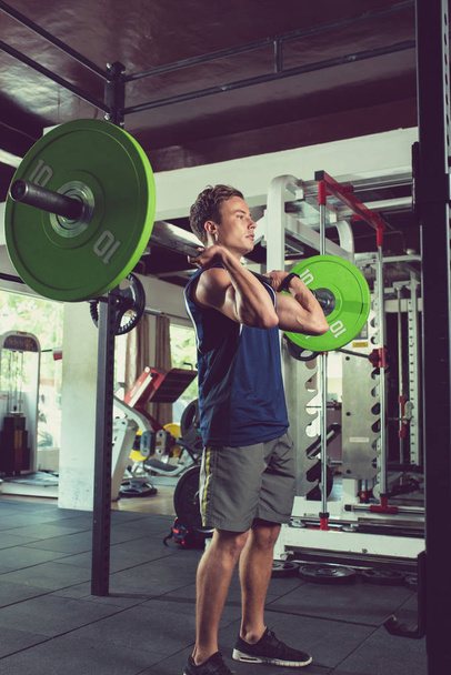 Fit young man lifting heavy barbell in gym - Photo, Image