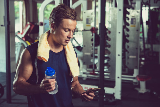 Fit man with water bottle reading message on smartphone - Photo, Image