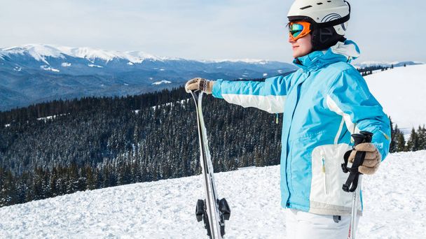 μια γυναίκα σε ένα μπλε κοστούμι, κράνος και γυαλιά στέκεται με σκι στην κορυφή ενός βουνού. - Φωτογραφία, εικόνα
