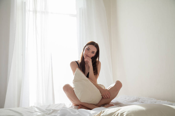 brunette vrouw na het slapen in slaapkamer kussens op het bed - Foto, afbeelding