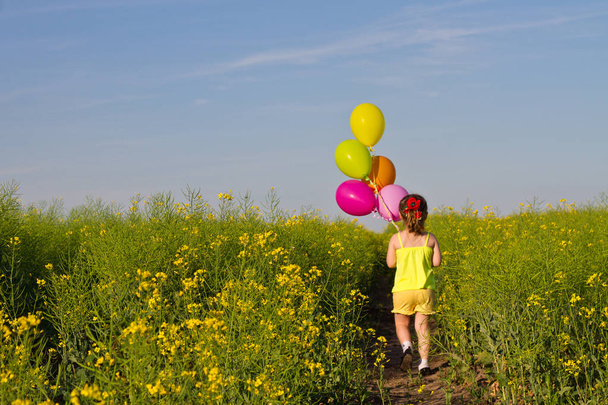 маленькая азиатка в платье бежит по зеленому пшеничному полю с воздушными шарами в руке, замедленное движение
 - Фото, изображение