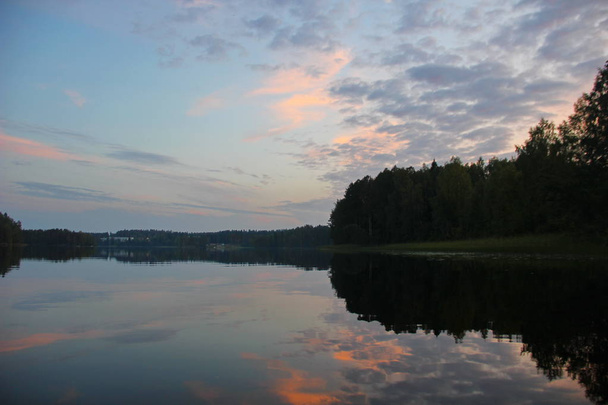 Sonnenuntergang über dem See, glattes Wasser, Spiegelung des Himmels, zarte rosa und blaue Farbtöne, Wald am Ufer, symmetrischer Rahmen, Natur Kareliens - Foto, Bild