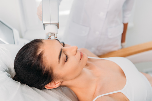 Teilansicht einer Frau, die im Wellness-Salon vom Kosmetologen eine stimulierende elektrische Gesichtsmassage erhält - Foto, Bild