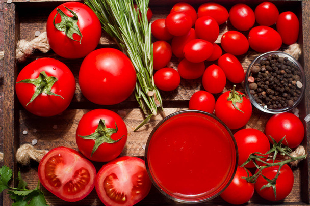 glass of organic tomato juice and fresh tomatoes with herbs on wooden tray, top view - Foto, afbeelding
