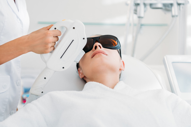 Frau mit Schutzbrille bekommt Laser-Haarentfernung von Kosmetikerin im Wellness-Salon - Foto, Bild