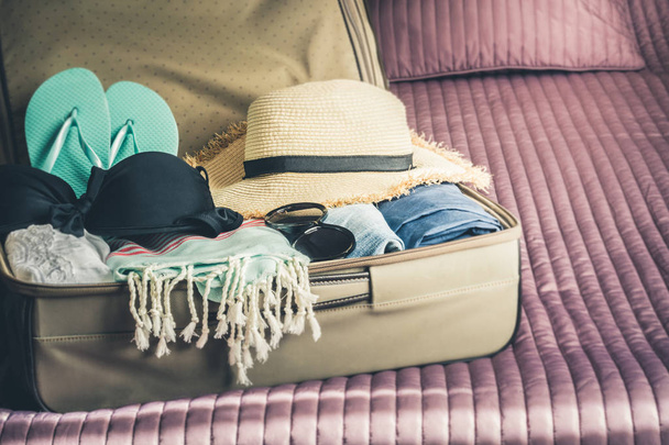 Offener Koffer mit Frauenkleidung für den Strandurlaub auf dem Bett. Dinge packen. - Foto, Bild