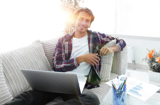 young man with a laptop sitting on a sofa near a coffee table - Photo, image