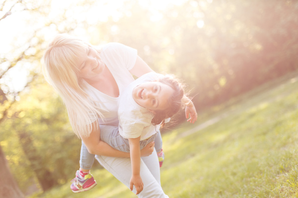 Young mom and cheerful adorable girl having fun together in park in summertime - Foto, Bild