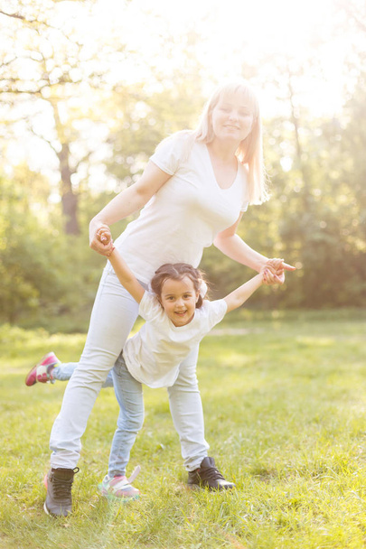 Young mom and cheerful adorable girl having fun together in park in summertime - Zdjęcie, obraz