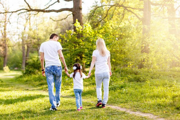 cute baby girl holding hands with parents walking in park, back view - Foto, Imagen