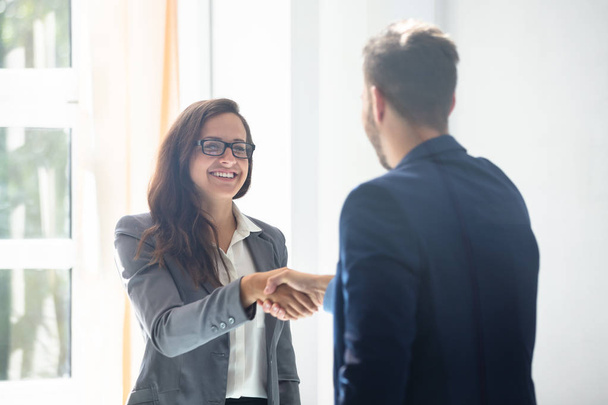 Smiling Young Businesswoman Shaking Hands With Her Partner In Office - Foto, afbeelding