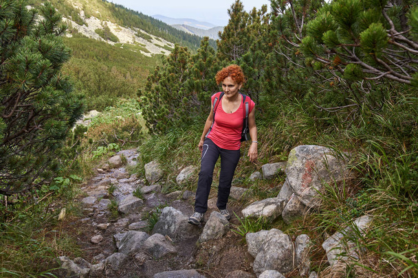 Middle aged woman with backpack hiking on trail in mountains at daytime - Foto, afbeelding