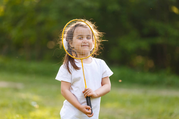 Schattig klein meisje spelen badminton buiten op warme en zonnige zomerdag - Foto, afbeelding