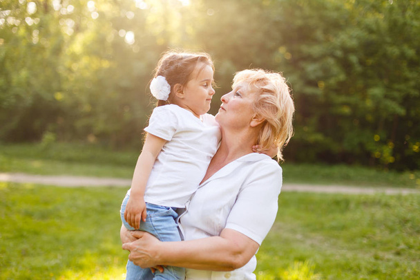 Grandmother carrying her little granddaughter and smiling standing outdoors - Photo, Image