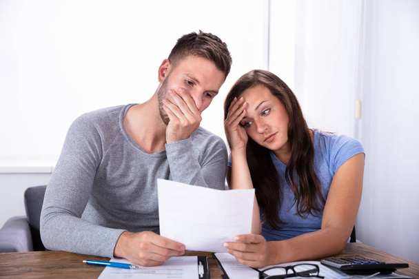 Portrait Of A Sad Young Couple Looking At Invoice - Фото, изображение