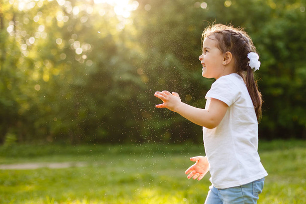 Linda chica rizada jugando con burbujas de jabón en el jardín verde. Concepto de infancia feliz
. - Foto, Imagen