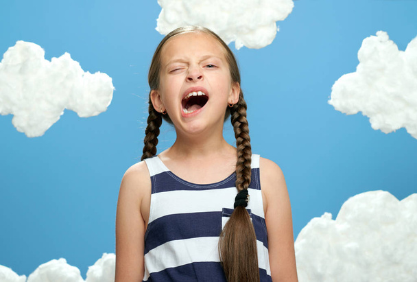 девушка в полосатом платье позирует на голубом фоне с хлопковыми облаками, концепция лета и счастья
 - Фото, изображение