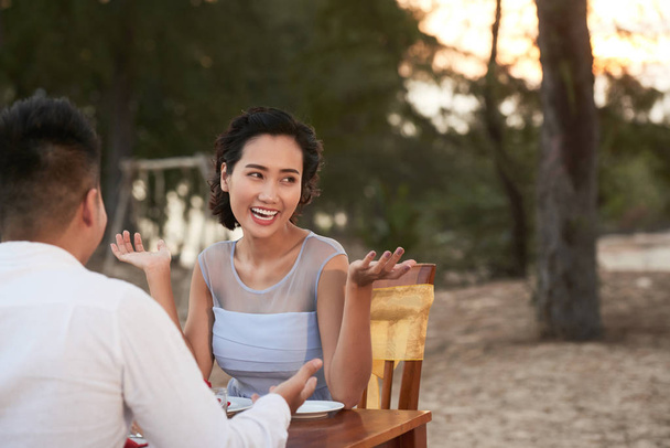 cheerful Asian woman having fun with loving boyfriend while enjoying breathtaking sunset at beach restaurant - Фото, изображение