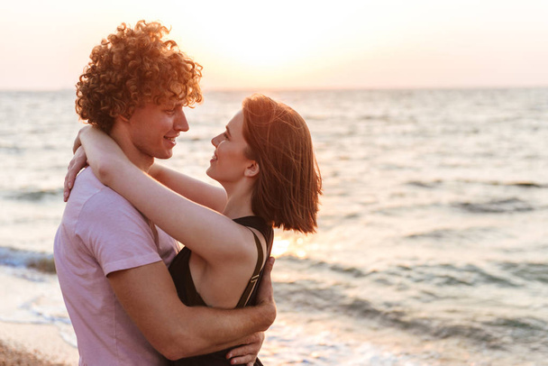 Портрет улыбающейся молодой пары, обнимающейся на пляже
 - Фото, изображение