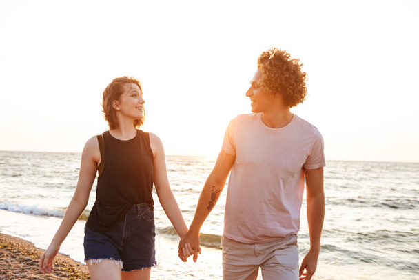 Picture of cute young loving couple walking outdoors on the beach. - Фото, изображение