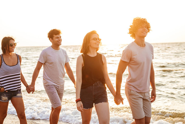 Image of excited group of friends loving couples walking outdoors on the beach having fun. - Фото, изображение