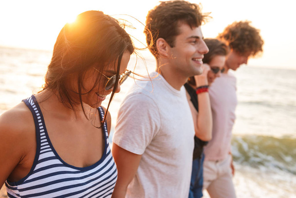 Picture of happy group of friends loving couples walking outdoors on the beach having fun. - Photo, image