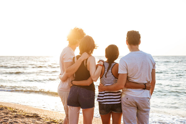 Back view picture of happy group of friends loving couples walking outdoors on the beach having fun. - 写真・画像