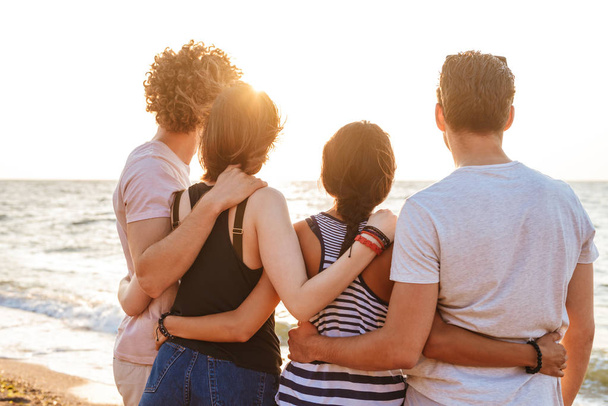 Back view picture of happy group of friends loving couples walking outdoors on the beach having fun. - 写真・画像