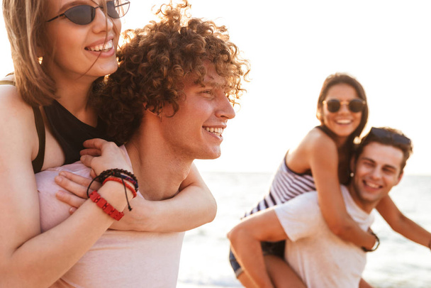 Picture of happy group of friends loving couples walking outdoors on the beach having fun. - Photo, image